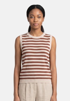 Young woman with black hair in a ponytail wears a sleeveless brown and beige striped top and beige pants, standing against a plain background.