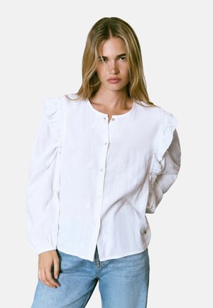 Blusa de algodón blanca con detalles de volantes en los hombros, cierre de botones, mangas largas y un sutil patrón texturizado. Tejido ligero y corte relajado.