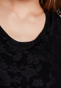 Schwarzes Spitzengewebe mit floralem Muster, rundem Ausschnitt und weicher Textur, geeignet zum Schichten oder als eigenständiges Kleidungsstück.