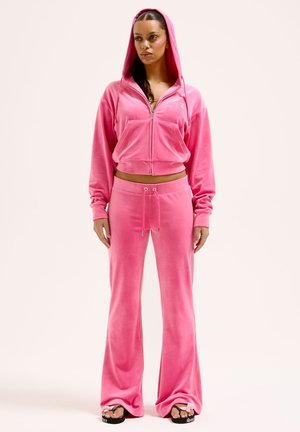 Roze velours trainingspak met een gezipte, cropped hoodie en broek met wijde pijpen. Voorzien van een voorzak en een tailleband met trekkoord. Soepele textuur.