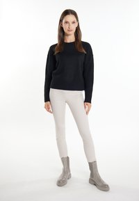 Pulover negru tricotat cu gât rotund; pantaloni ajustați bej deschis; cizme gri până la gleznă cu talpă groasă și panouri laterale elastice.