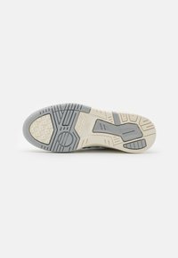 Semelle de chaussure avec une surface en caoutchouc gris et des accents crème. Présente des motifs texturés et des rainures pour une adhérence et un soutien accrus.