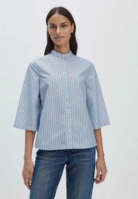 Camicia colletto in azzurro chiaro con righe verticali. Presenta maniche a tre quarti e chiusura con bottoni sul davanti. Realizzata in tessuto morbido.