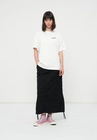 Camiseta blanca de algodón con mangas cortas y un pequeño estampado; falda negra con bolsillos; zapatillas altas rosas; diseño minimalista.