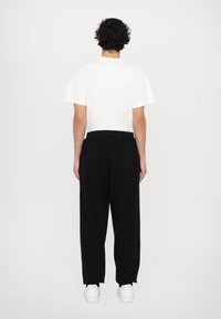 White short-sleeve t-shirt paired with black relaxed-fit pants. The pants feature an elastic waistband and are styled with white sneakers.