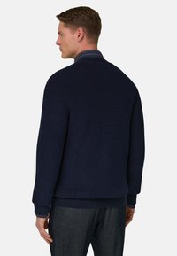 Maglione blu navy a coste con colletto alto, realizzato in tessuto strutturato e vestibilità comoda. Polsini e orlo evidenziati, indossato sopra una camicia di jeans.