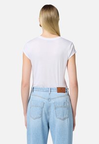 Camiseta blanca de manga corta con una textura suave, combinada con unos jeans de mezclilla celestes de cintura alta que presentan una etiqueta de cuero marrón y bolsillos.