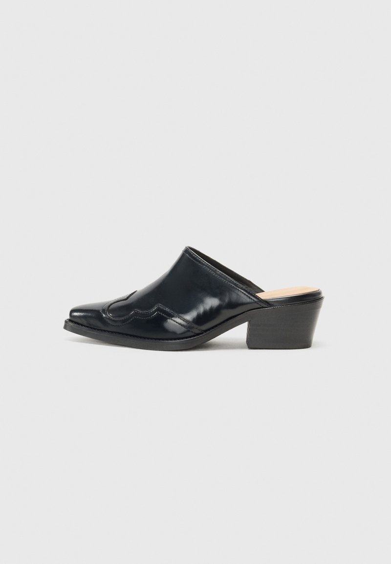 Mules de pele patentada preta com ponta fina, um design curvado e um salto quadrado baixo, apresentando costura decorativa ao longo da parte superior.