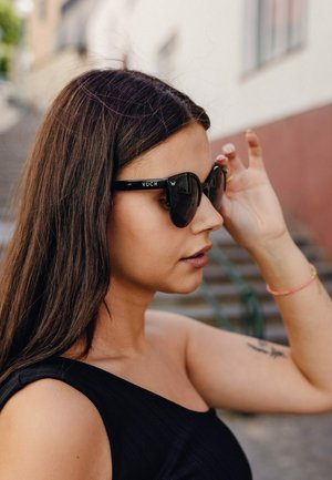 Černé sluneční brýle ve stylu kočičích očí s lesklým povrchem, na obroučkách s bílým logem "VUCH" a texturovaným povrchem, doplněné černým topem.