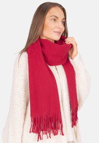 Roter Schal aus weichem Material mit fransigen Enden, um den Hals gewickelt, kombiniert mit einem strukturierten weißen Pullover.