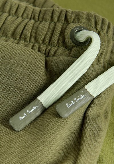 Nærbillede af olivengrøn elastisk taljebånd med hvid snor med mærkede ender på blødt stof.