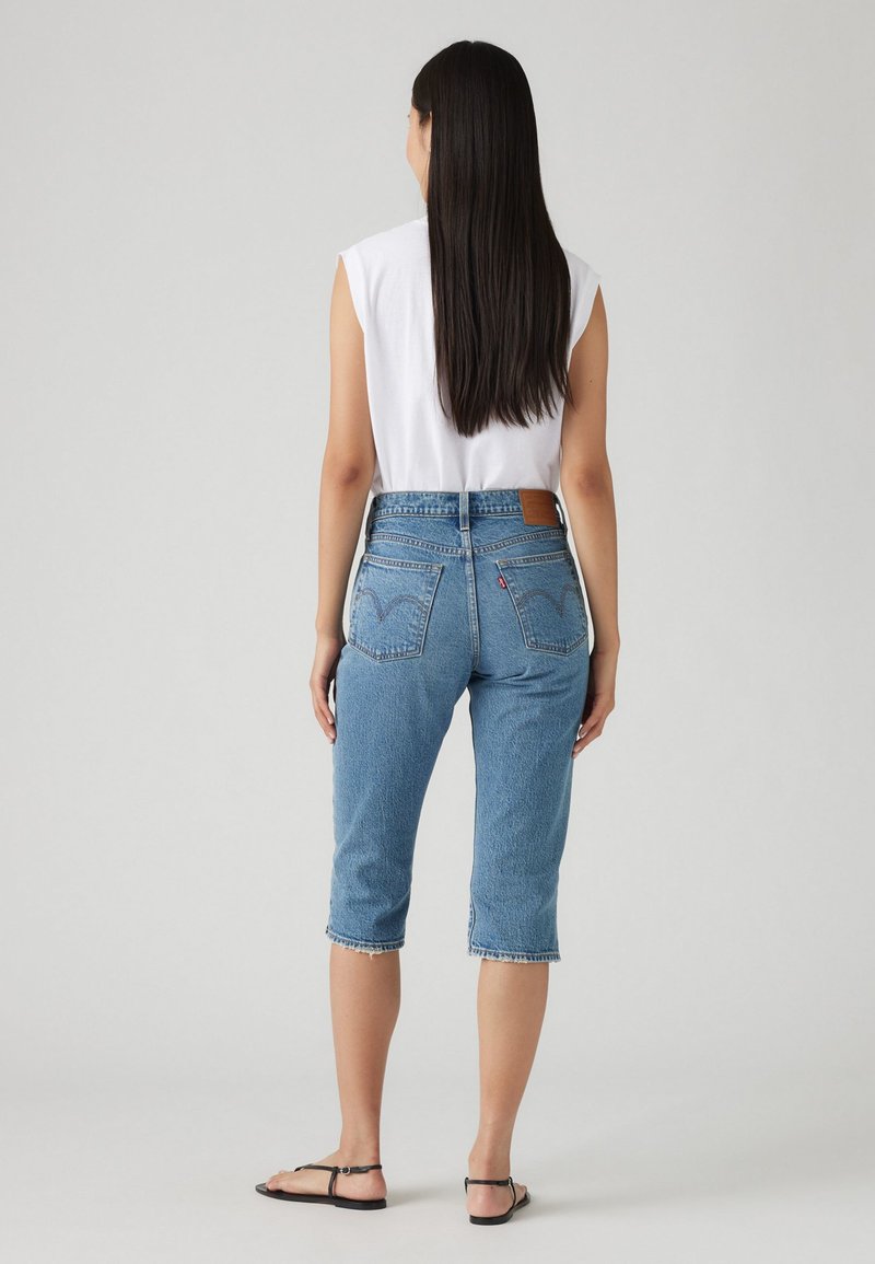 Jean capri en denim bleu clair avec une taille haute, un ourlet effiloché et des poches arrière arborant un patch de logo classique.