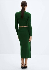 Ensemble à deux pièces en maille côtelée verte comprenant un crop top à manches longues et une jupe midi. Caractéristiques : coupe ajustée et fente sur le côté de la jupe. Talons noirs.