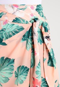Růžovo-oranžová sukně s zelenými tropickými listy a růžovými květy, s předním uzlem uvázaným v pase.