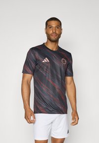 T-shirt de sport graphique foncé avec des motifs abstraits rouges et bleus, à manches courtes, avec un col rond et un logo brodé sur la poitrine.
