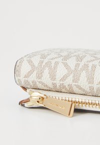 Portafoglio bianco con zip, caratterizzato da un motivo testurizzato, hardware in tonalità oro e una finitura in tessuto liscio, con il logo del marchio sul cursore della zip.