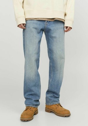 Jean droit bleu clair associé à des bottines de travail lacées couleur sable et un sweat crème, visible de la taille aux pieds.