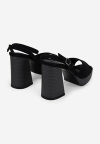 Sandalias de tacón alto de ante negro con punta abierta, diseño de tira trasera y tacón cuadrado texturizado. El tacón cuenta con estrías verticales para mayor agarre.