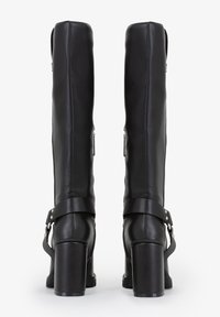 Stivali in pelle nera al ginocchio con tacco a blocco, caratterizzati da una cintura attorno alla caviglia con dettagli in metallo e una chiusura lampo laterale.