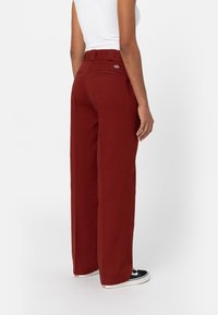 Bredbenta, rostfärgade byxor med hög midja, bältesloopar, bakficka och minimalistisk design. Matchas med svarta sneakers.