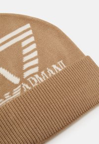 Beanie in maglia marrone con risvolto, motivo grafico bianco e dettaglio testuale. Realizzato in morbido tessuto testurizzato per calore e comfort.