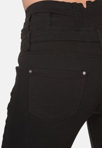 I jeans in denim nero presentano un design aderente, una cintura testurizzata e tasche posteriori con borchie argento e cuciture visibili.