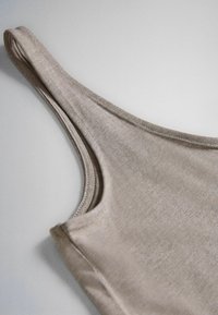 Beige ærmeløs tanktop med rund halsudskæring, lagt fladt på en lys overflade, som viser stoffets struktur og syningsdetaljer.