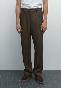 Brown linen trousers with a straight-leg design, front pockets, and a single button closure, paired with dark brown shoes.