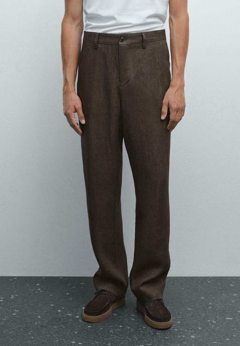 Brown linen trousers with a straight-leg design, front pockets, and a single button closure, paired with dark brown shoes.