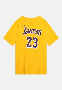 Keltainen puuvillapaita lyhyillä hihoilla, jossa etuosassa lukee "LAKERS" violetilla ja numero "23" valkoisella ja violetilla. Kauluksessa on Nike-logo.