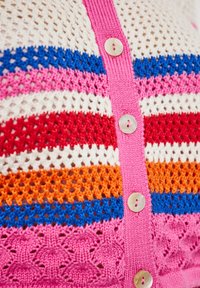 Közelkép egy kötött kardigánról, amely vízszintes csíkokkal rendelkezik kék, rózsaszín, fehér, piros, narancssárga színben, és négy bézs gomb található a rózsaszín gombolón.