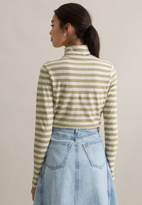 Bluzka w paski z długim rękawem w stonowanej zieleni i bieli, z wysokim kołnierzem. Połączona z jasnoniebieską, wysoką spódnicą jeansową z kieszeniami.