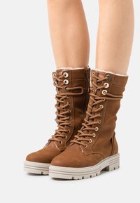Bottes en cuir marron à lacets avec une finition texturée, dotées d'une doublure douce et d'une semelle épaisse de couleur claire. Fermeture éclair sur le côté pour une mise en enjambement facile.