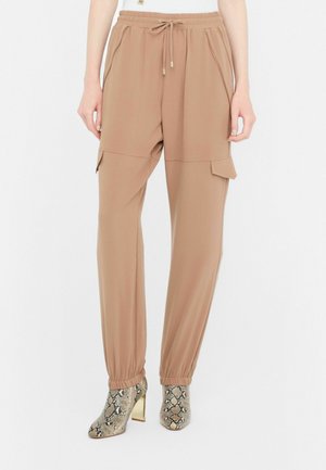 Light brown cargo pants with an elastic waistband, side pockets, and cuffs at the ankles, paired with snakeskin-patterned heels.