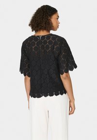 Top in pizzo nero con motivo floreale, orlo a scallop e maniche corte. Sul retro presenta un'apertura a occhiello con chiusura a bottone.