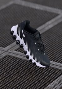 Zwarte sportieve schoen met een glad bovenwerk, contrasterende witte accenten en ronde zwarte zoolpods. Ontworpen voor comfort en prestaties.
