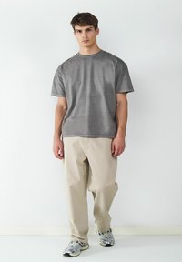 Szara koszulka z krótkim rękawem, luźny krój, w połączeniu z kremowymi spodniami i szarymi trampkami. Prosty design, minimalne detale.