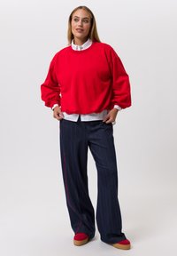 Rode oversized trui met opgeblazen mouwen, gecombineerd met donkere gestreepte broek met een rode zijstreep. Model draagt rode plateauzolen.