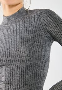 Gray ribbed knit sweater with a high neckline, featuring a fitted design and textured fabric. Close-up view highlights the ribbing pattern.