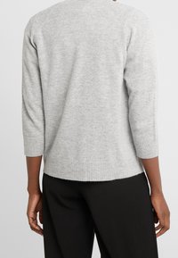 Pull en maille grise avec manches trois-quarts, poignets et ourlet côtelés, doté d'une texture douce et d'une coupe décontractée, vu de dos.