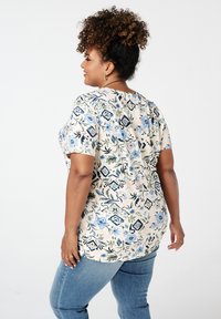 Bloemige blouse met korte mouwen op een crèmekleurige achtergrond, met blauwe en groene patronen. Zachte stof, losse pasvorm en ronde halslijn.