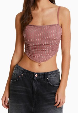 Haut court froncé rose avec des clous argentés, muni de fines bretelles et d'un décolleté carré, associé à un jean en denim foncé taille haute.