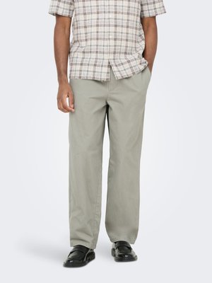 Man wearing light gray wide-leg pants, black loafers, and a short-sleeve beige and gray plaid button-up shirt.