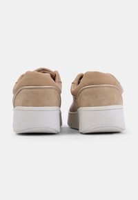 Beige sportcipő sima bőr felsőrésszel és puha velúr részletekkel, fehér gumitalppal és párnázott sarkal.