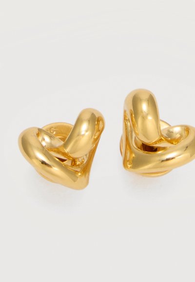 Par de pendientes de botón de nudo torcido dorados y brillantes sobre un fondo claro y liso.