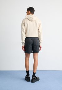 Beige hoodie with a drawstring and kangaroo pocket, paired with black shorts featuring an elastic waistband, set against a light backdrop.