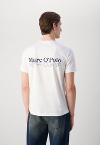 Hvid bomulds t-shirt med "Marc O'Polo" tekst i marineblå på ryggen. Klassisk crew neck, korte ærmer og en afslappet pasform.