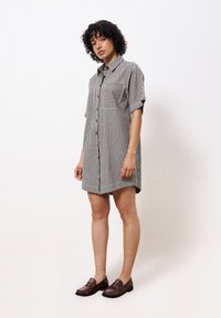 Gestreiftes Hemdkleid mit kurzen Ärmeln, das zwei Vorderstaschen und eine lockere Passform aufweist. Das Material wirkt weich mit einer subtilen Textur.