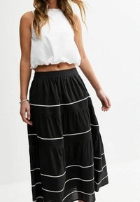 Musta kerroksellinen maxi-hame, jossa on valkoiset ompeleet, yhdistettynä valkoiseen lyhytleikkaukseen tanktoppiin, esittelee rentoa ja hengittävää muotoilua.