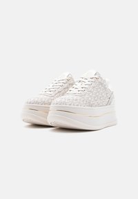 Άσπρα sneakers με πάτο πλατφόρμας, ανοιχτογκρι γεωμετρικό σχέδιο, χρυσές λεπτομέρειες και άσπρα κορδόνια σε απλό λευκό φόντο.